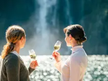 Two guests enjoying drinks with views of Milford Sound.