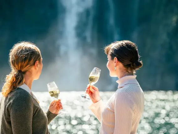 Two guests enjoying drinks with views of Milford Sound.