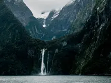 Waterfall cascading between steep mountains into Milford Sound.