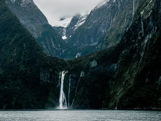Waterfall cascading between steep mountains into Milford Sound.