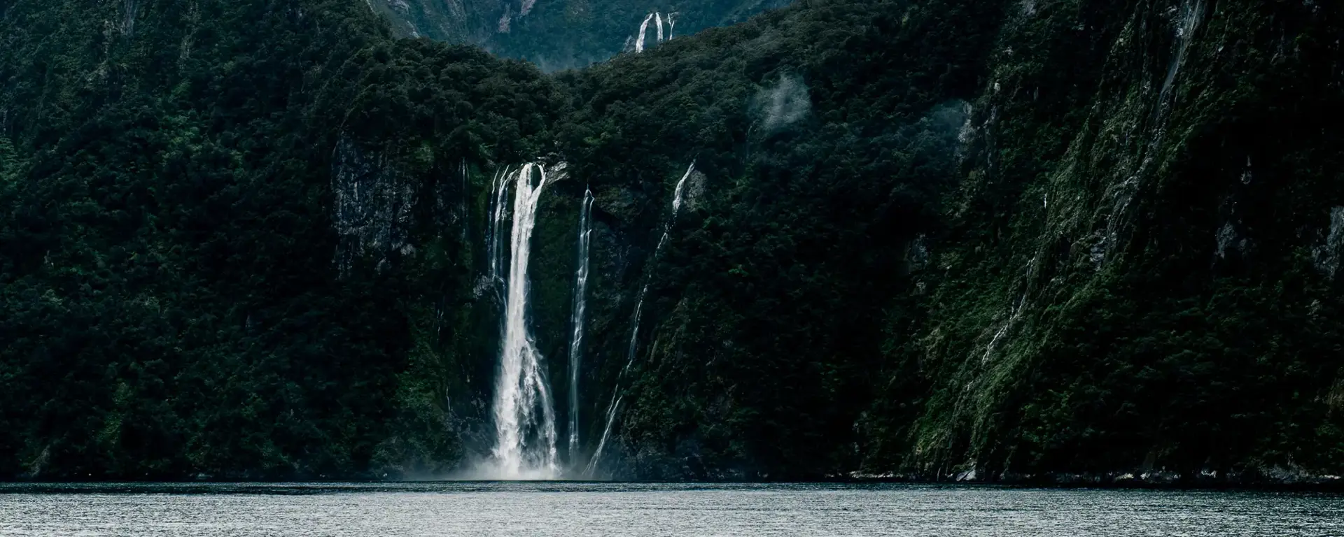 Waterfall cascading between steep mountains into Milford Sound.