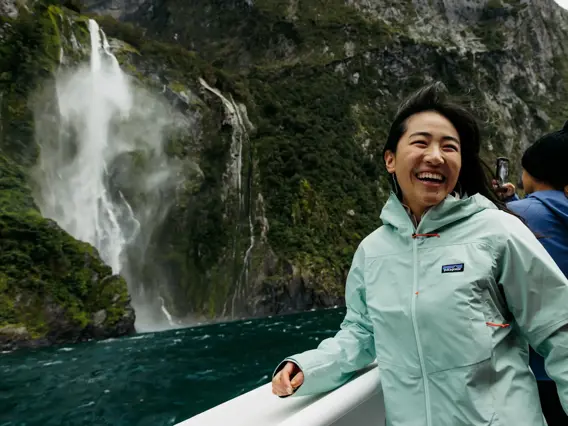 Friends enjoying a Milford Sound day cruise near a waterfall.