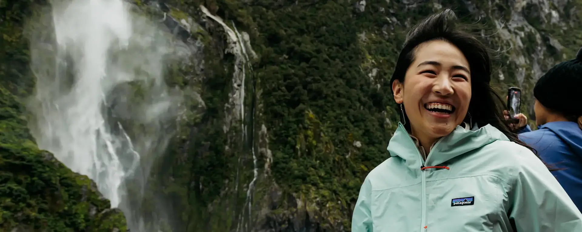 Friends enjoying a Milford Sound day cruise near a waterfall.