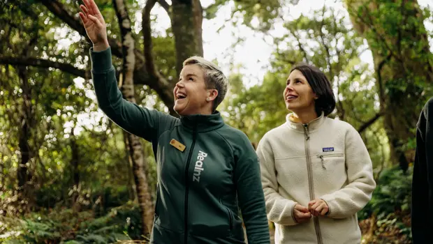 A RealNZ nature guide points out something to a guest in the trees of Ulva Island, on a guided walk through the forrest. 