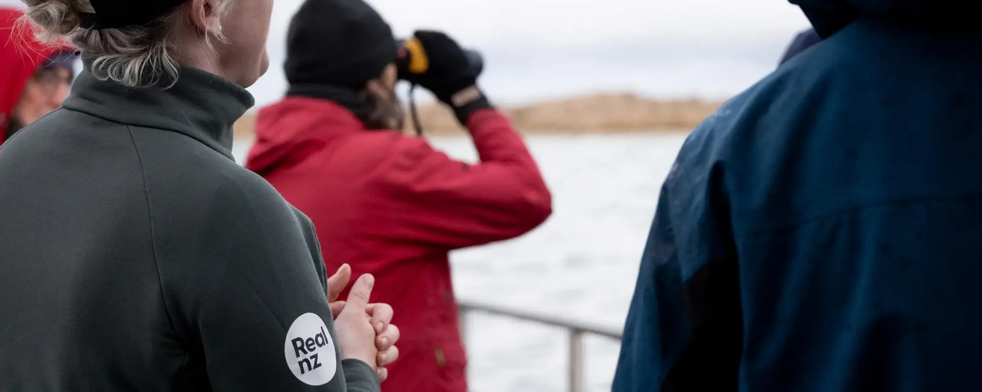 A group of guests try to spot wildlife from a cruise boat, one using binoculars. 