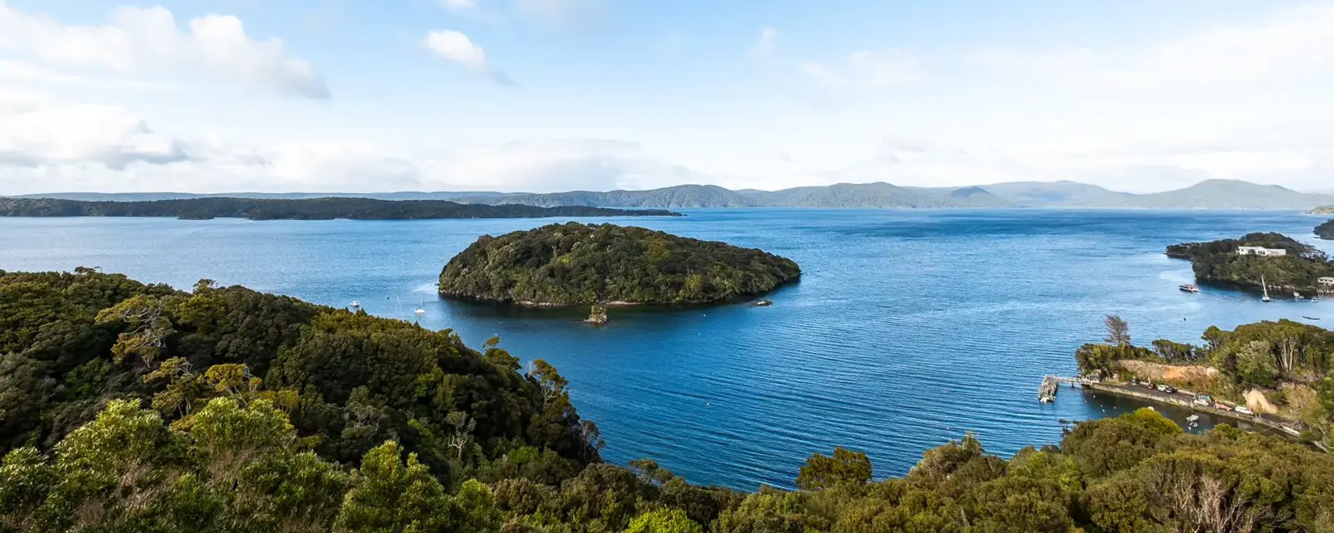 Lookout view of a lush green forrest island in the middle of clear blue ocean water.