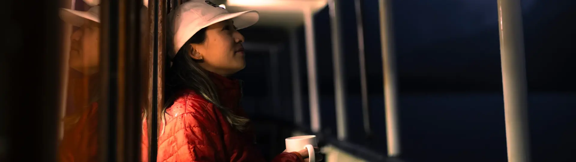 Woman holding a mug on the deck of a boat at dusk.