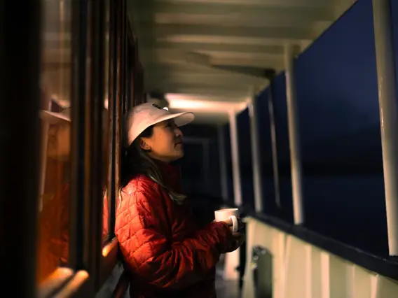 Woman holding a mug on the deck of a boat at dusk.