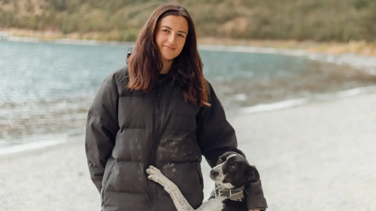 Headshot of a woman standing outside by a lake, with a border collie jumping up to lean on her.