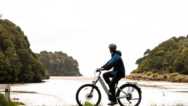Cyclist riding an e-bike beside a peaceful coastal inlet.