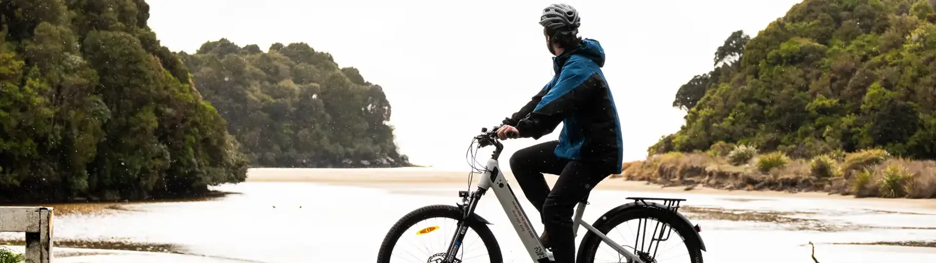 Cyclist riding an e-bike beside a peaceful coastal inlet.