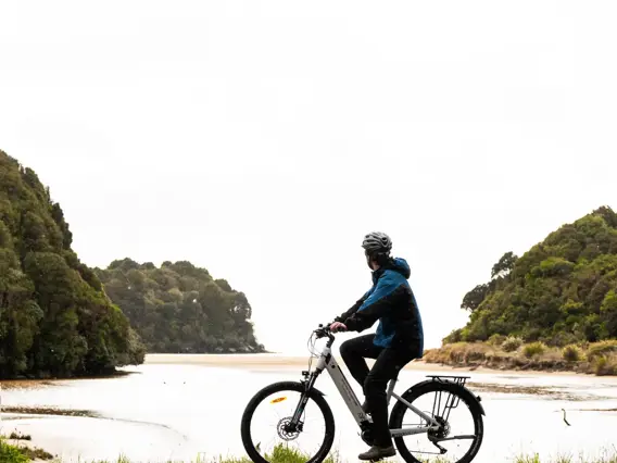 Cyclist riding an e-bike beside a peaceful coastal inlet.