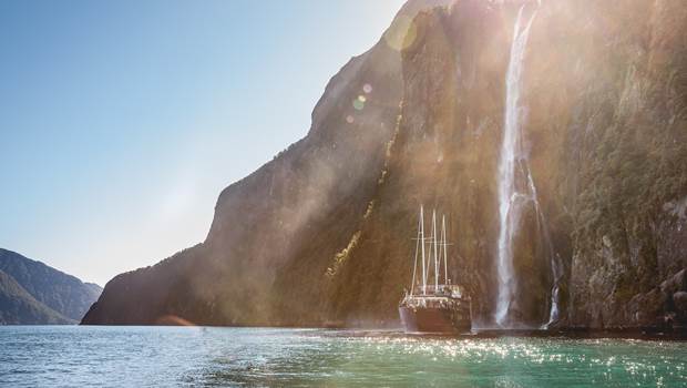 Boat under waterfall in Milford Sound