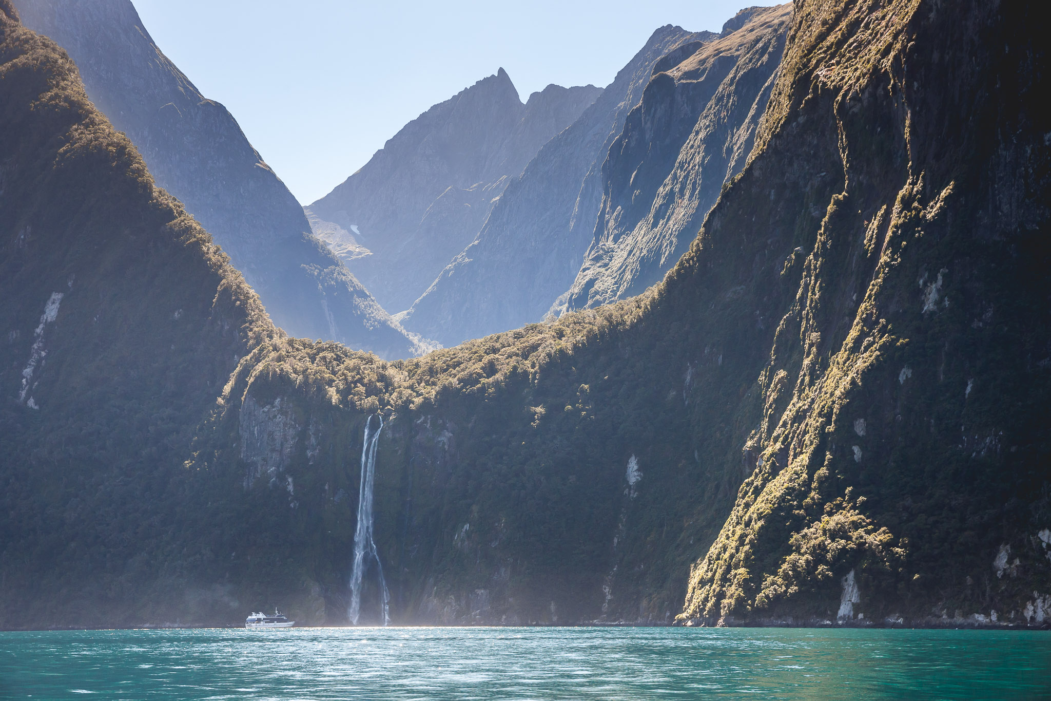 Boat in distance approaching waterfall in Milford Sound