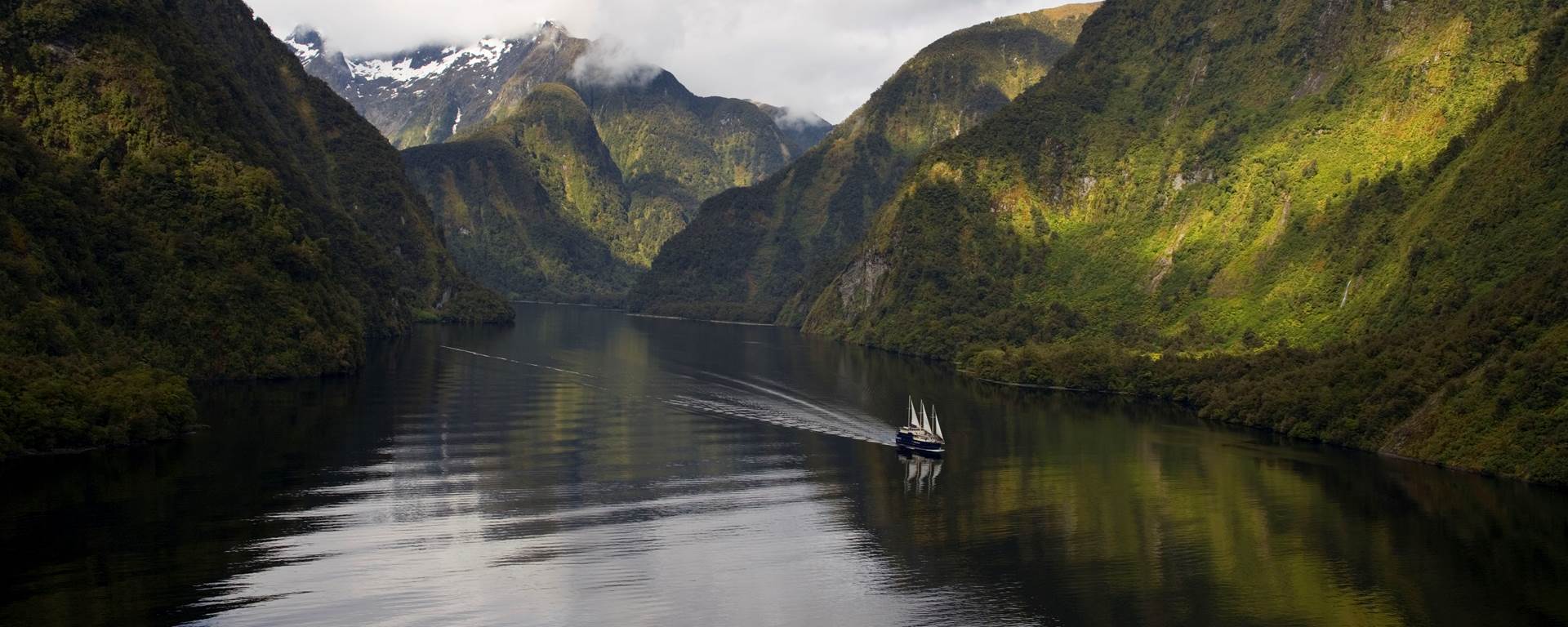 Boat sailing on the still waters of Doubtful Sound surrounded by lush mountains