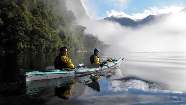 Two kayakers in Doubtful Sound on a misty day