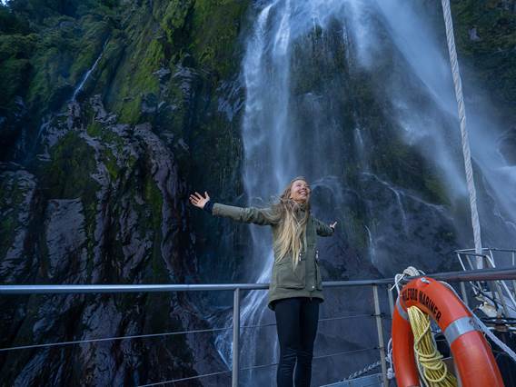 Woman stands under waterfall in Milford Sound