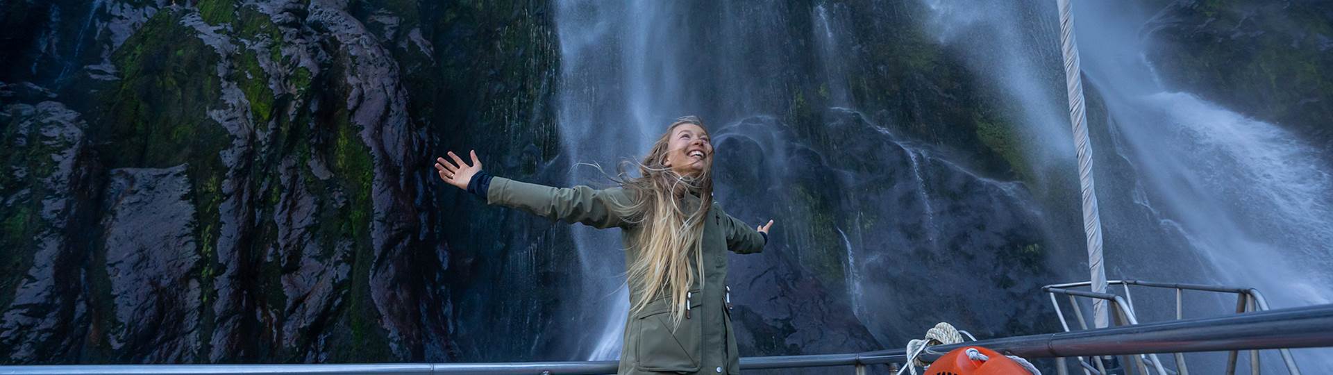 Woman stands under waterfall in Milford Sound