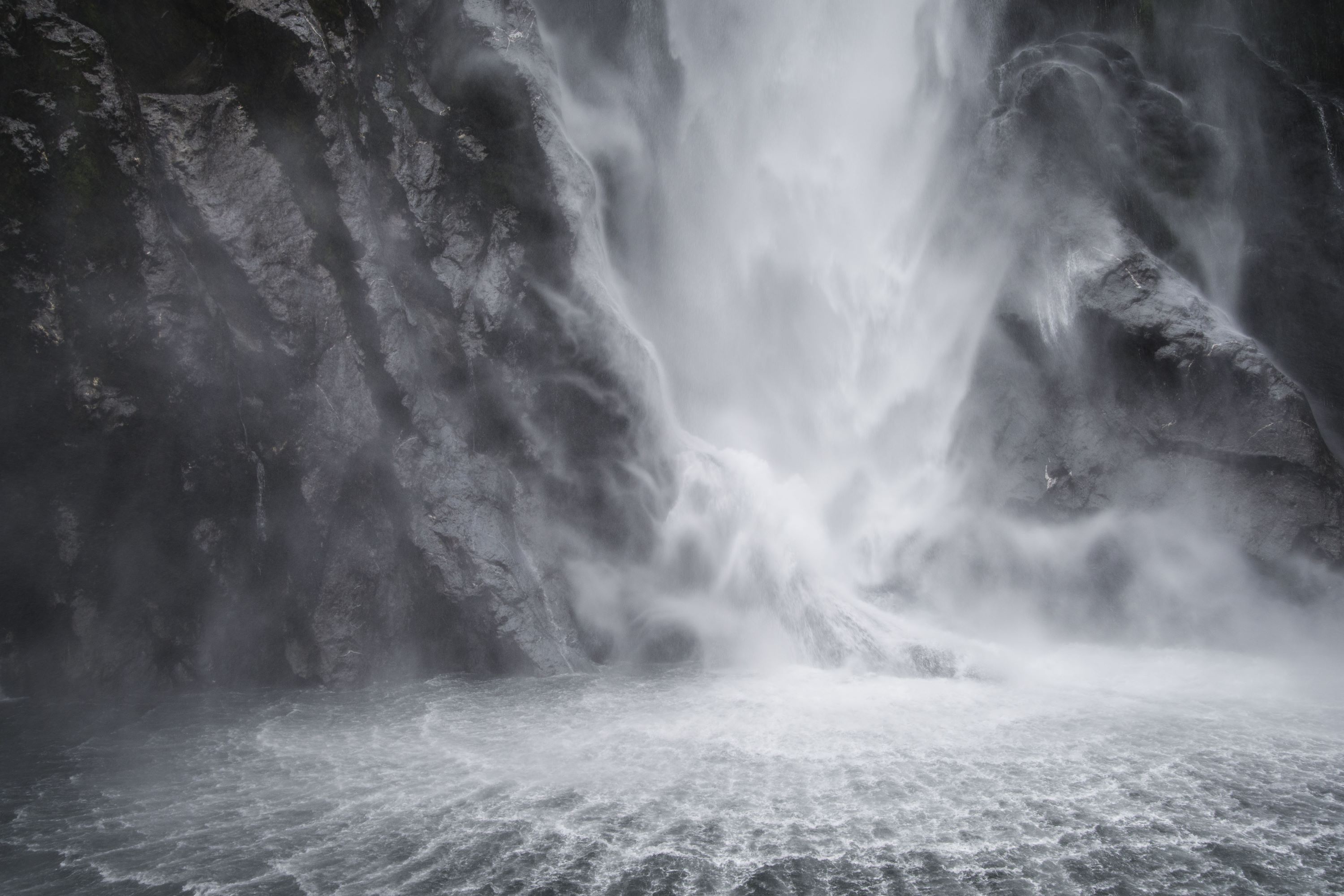 A dramatic waterfall causes spirals in the water at Milford Sound