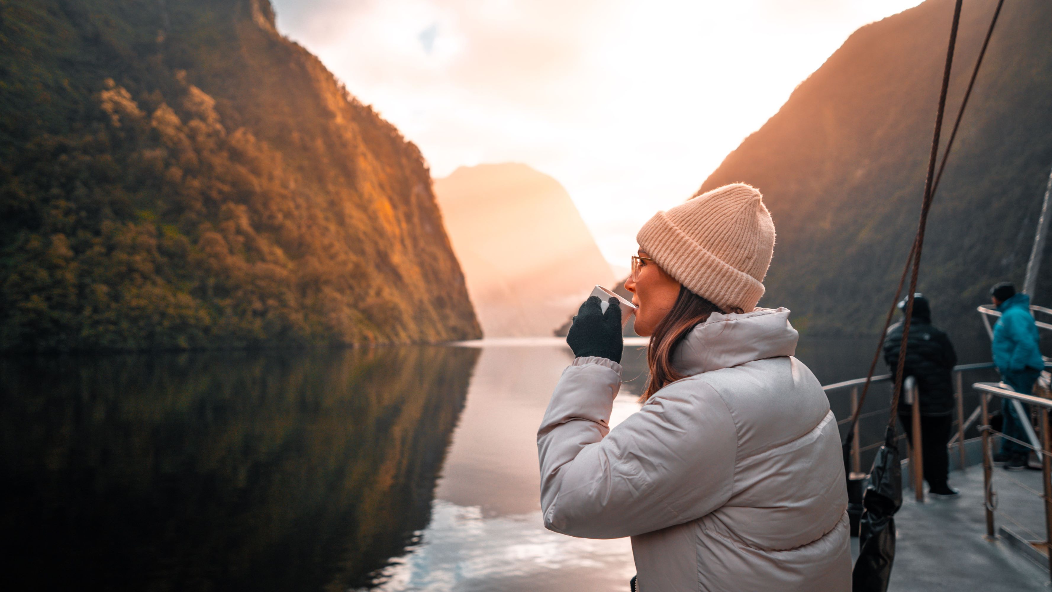 Women enjoys a hot drink outside in the winter sunrise at Doubtful Sound