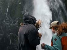 Two people getting sprayed by a waterfall in Milford Sound