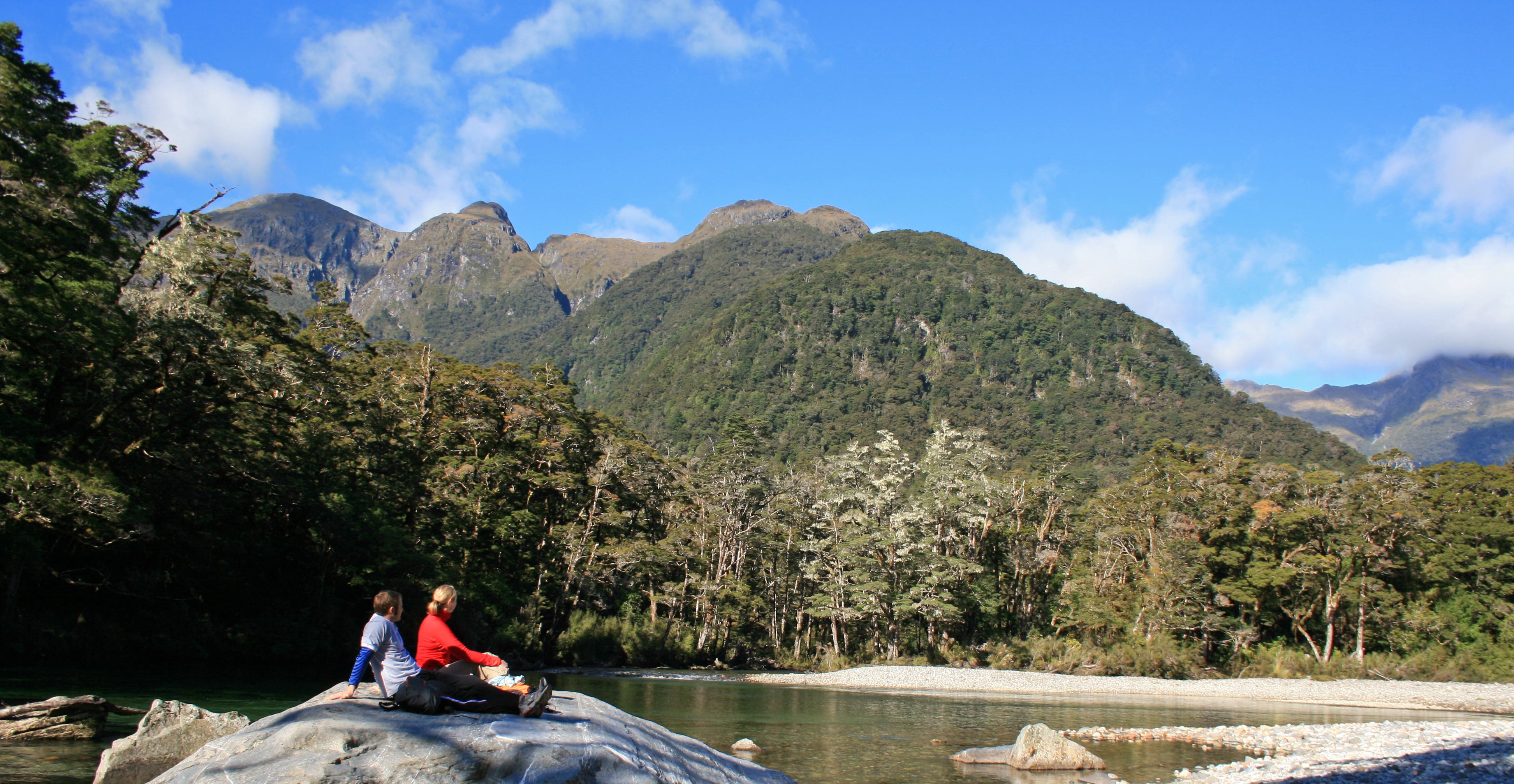 Two walkers sit on a rock on the Milford Track