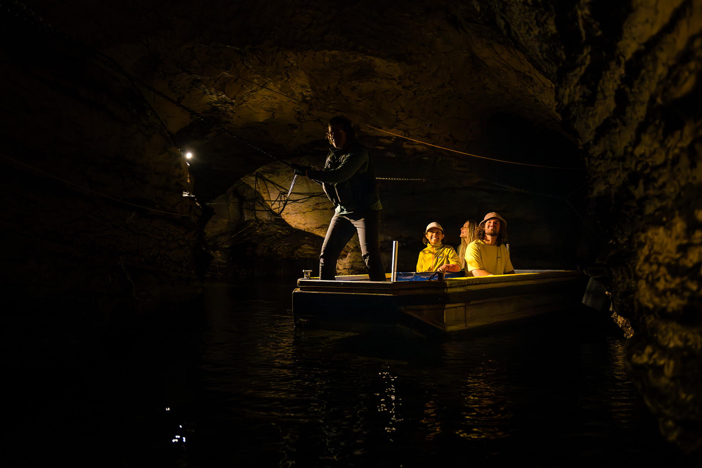 A group of three are guided through an underground cave on a small boat 