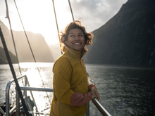 A woman smiles on the front deck of a boat cruising Milford Sound, with the sun setting behind