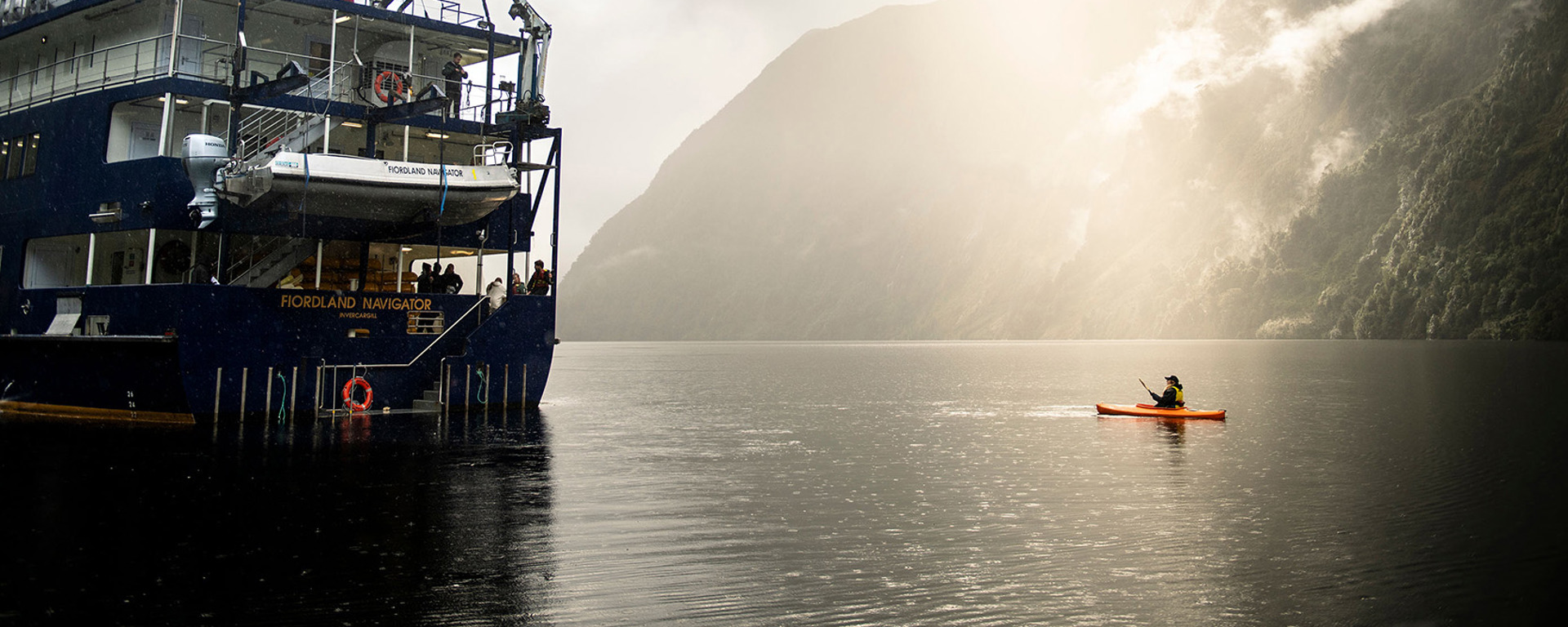 A kayaker floats near the Fiordland Navigator boat on the water at Doubtful Sound