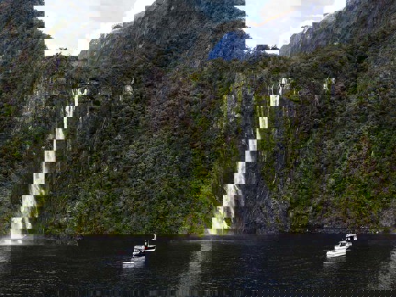 Wide shot of The Sovereign boat cruising in front of a waterfall on Milford Sound