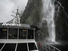 A close shot of The Sovereign boat cruising under a waterfall in Milford Sound