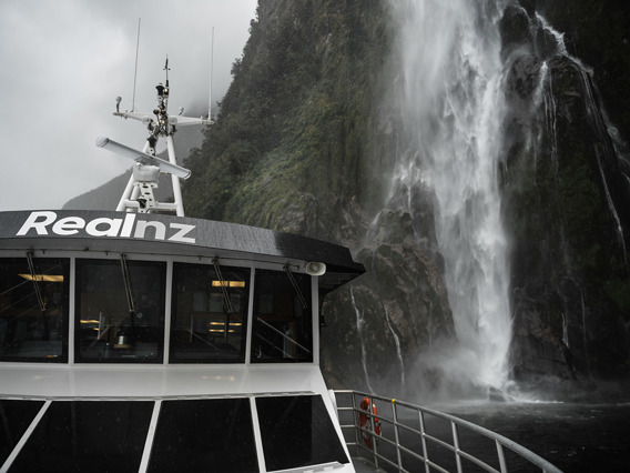 A close shot of The Sovereign boat cruising under a waterfall in Milford Sound