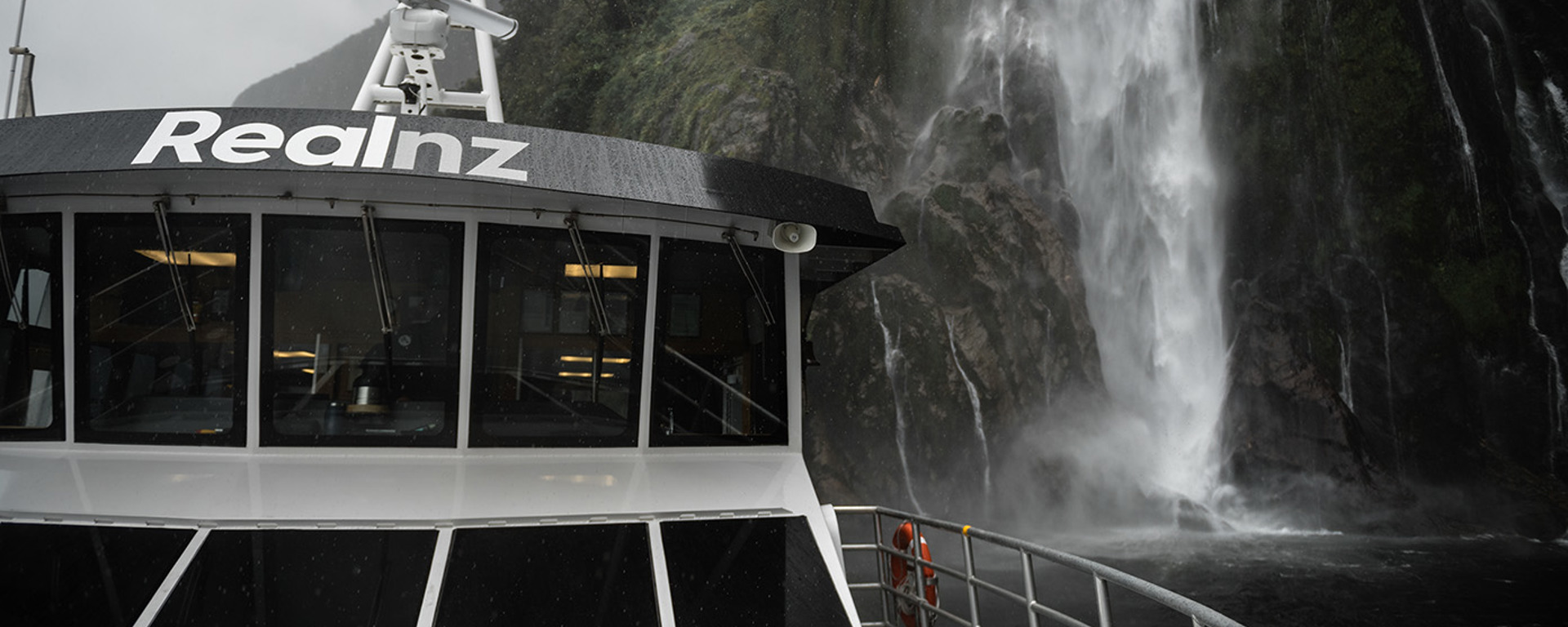 A close shot of The Sovereign boat cruising under a waterfall in Milford Sound
