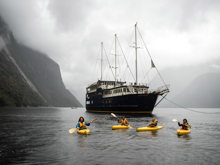 A group of four kayakers floating on Milford Sound in front of the Milford Wanderer boat. 