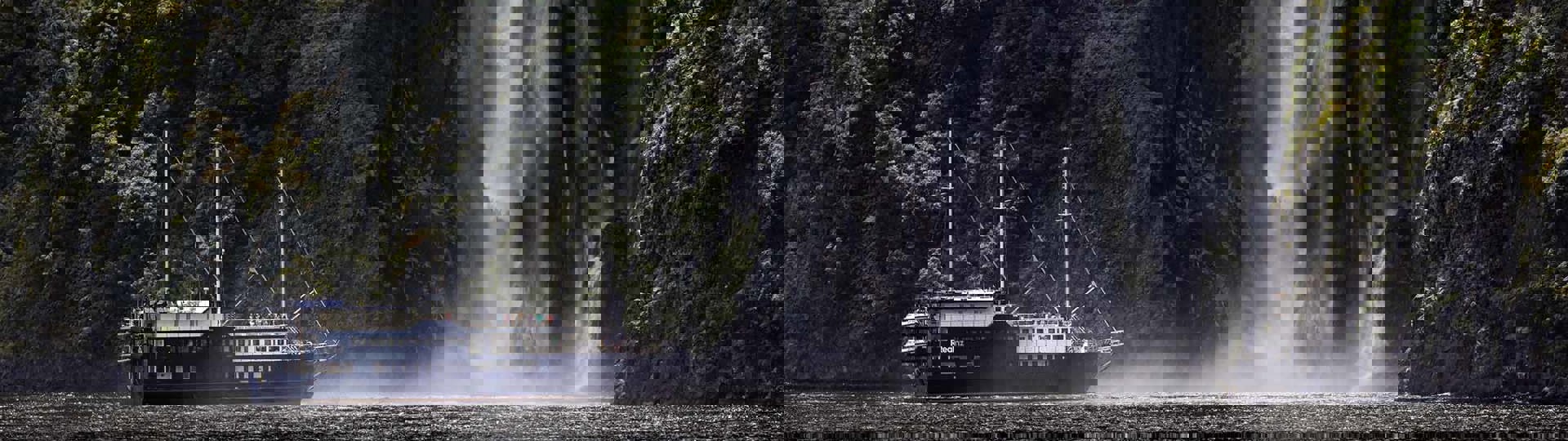 The Milford Mariner boat cruises close to a cascading waterfall in Milford Sound