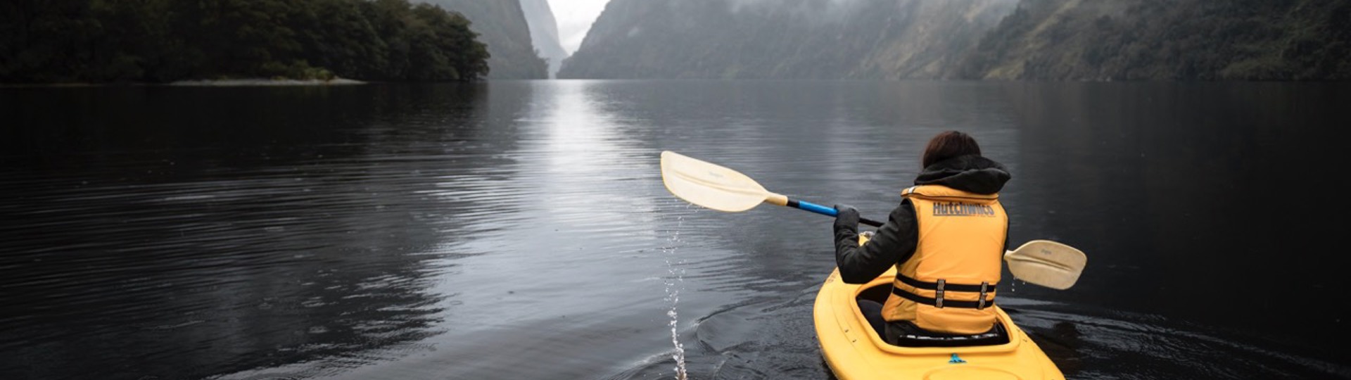 A bright yellow kayak floats along the water in gloomy Doubtful Sound 