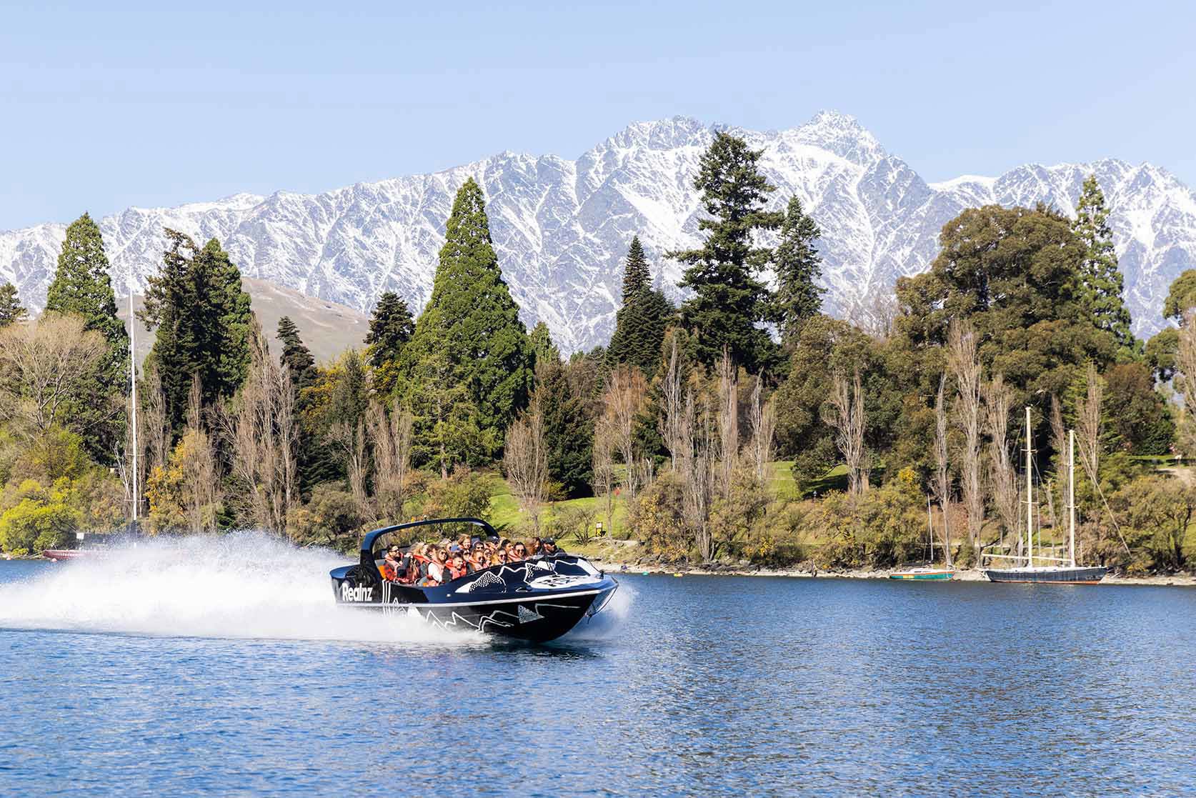 A queenstown jetboat zooms past the remarkables mountain range
