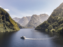 Wide shot of a motorised boat cruising through Doubtful Sound on a bluebird day