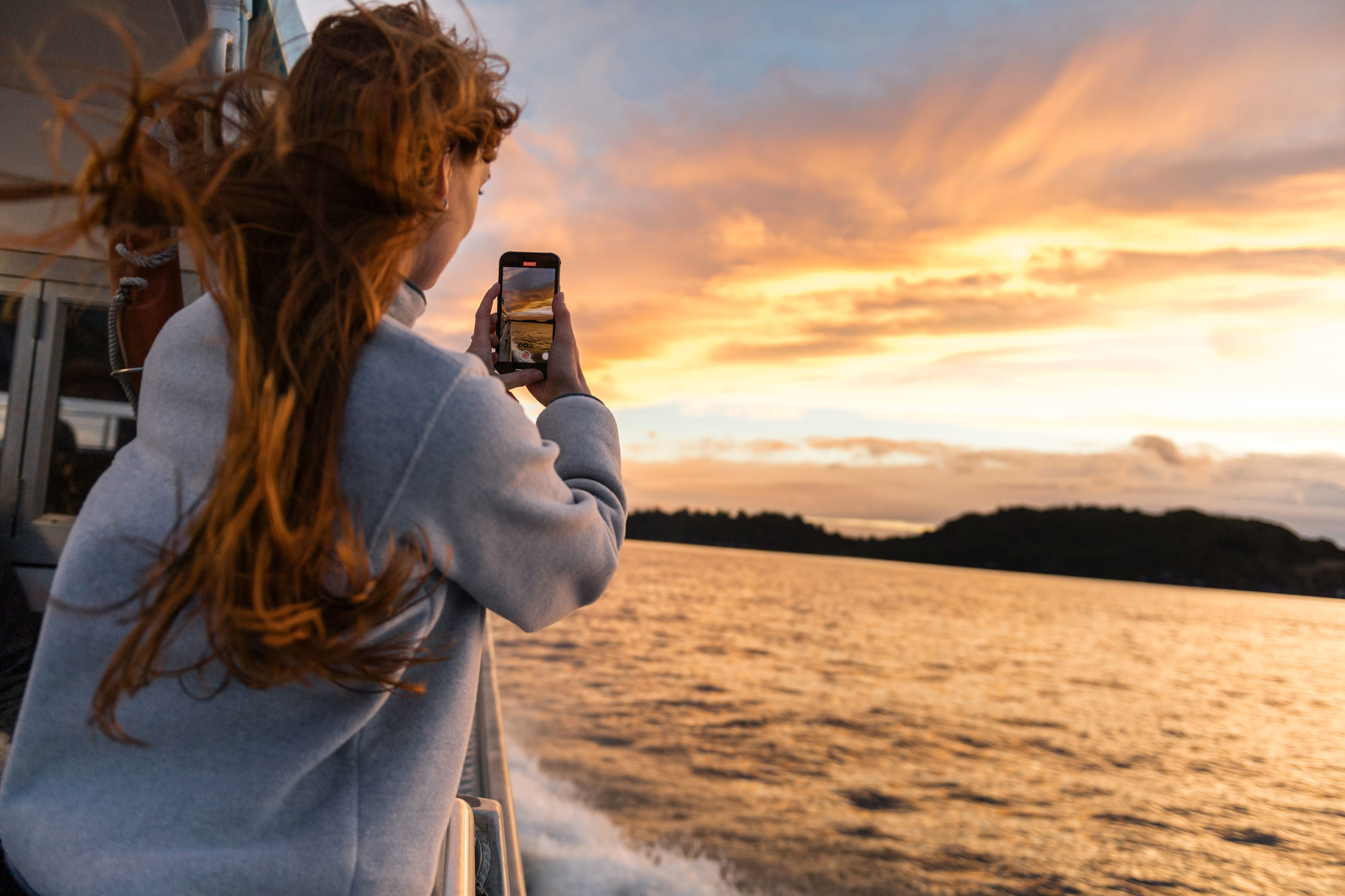 Woman taking photo on ferry at sunset