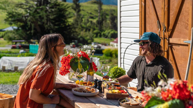 A couple enjoys a vibrant meal at Walter Peak’s Eco Experience, surrounded by stunning greenery, flowers, and mountain views.