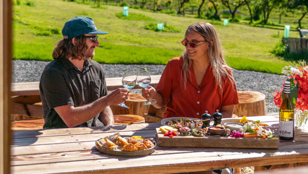 A couple toasts with wine at Walter Peak’s Garden to Table Experience, enjoying fresh platters and a serene orchard setting.