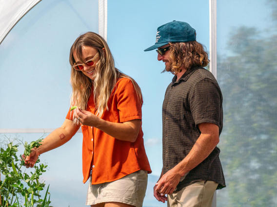 A couple explores Walter Peak’s Garden to Table Experience greenhouse, harvesting fresh vegetables and enjoying a hands-on sustainable experience.