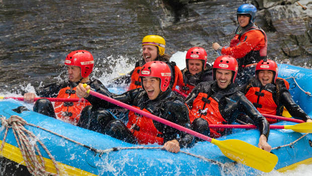 Group of excited rafters laughing and paddling as they ride through splashing rapids on the Shotover River in New Zealand.