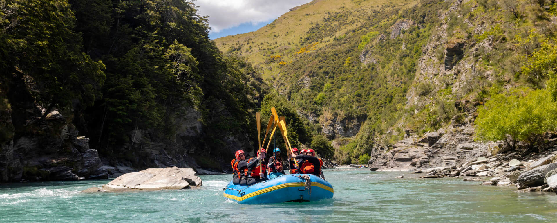 Rafters celebrating with paddles raised high while drifting through a serene canyon on the turquoise waters of the Shotover River.