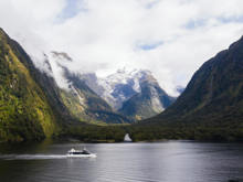Wide shot of a boat cruising in Milford Sound with snow covered mountains in the background