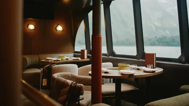 Elegant dining lounge with large panoramic windows overlooking a mountain landscape, featuring comfortable seating and set tables.