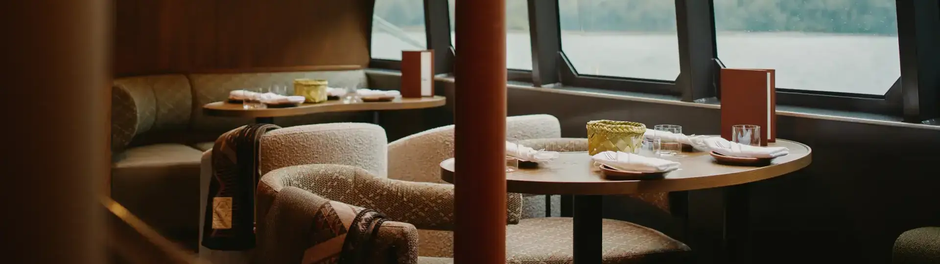 Elegant dining lounge with large panoramic windows overlooking a mountain landscape, featuring comfortable seating and set tables.