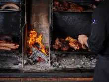 A chef standing at an indoor open fire BBQ tending to an assortment of meats. 