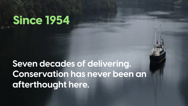 A vessel on a calm river surrounded by misty forested hills, with text reading "Since 1954 – Seven decades of delivering. Conservation has never been an afterthought here."
