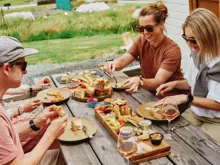 A group of friends enjoy shared platters of food and glasses of wine outside surrounded by green rolling hills.